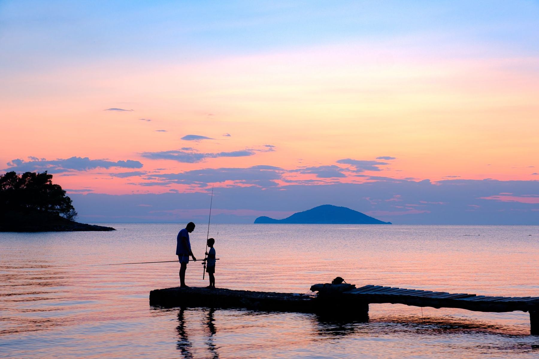 Two silhouettes fishing from a pier at sunset