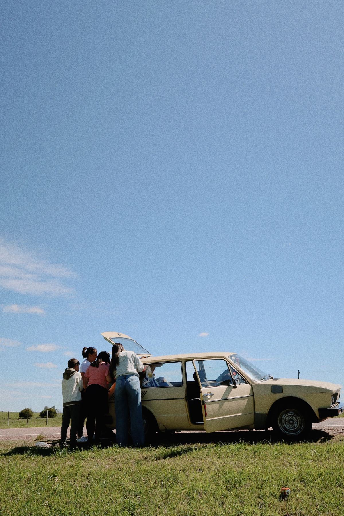 A family stopped beside a vintage car on a road trip